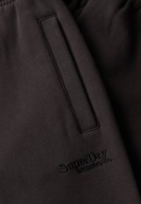 Pantalones deportivos negros con una textura suave, que cuentan con una cintura elástica acanalada y un logo bordado tonal en la parte delantera.