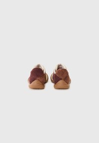 Adidași din suede maro, cu o formă rotunjită, având un accent la spate și tălpi din cauciuc. Căptușiți cu țesătură bej. Design simplu, în două nuanțe.