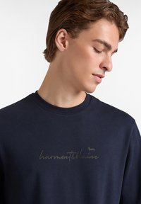 Sudadera navy con cuello redondo y textura suave, que presenta un sutil logo bordado en un tono contrastante a lo largo del pecho.