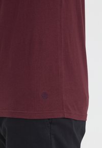 Burgunderfarvet bomulds t-shirt med et diskret logo broderet i marineblå ved kanten, med korte ærmer og en afslappet pasform.