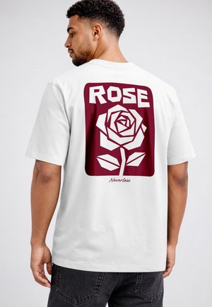 Mann, der mit dem Rücken zur Kamera steht, trägt ein weißes T-Shirt mit einer kastanienbraunen Grafik einer stilisierten Rose und dem Text "ROSE" und "Neverless" auf dem Rücken.
