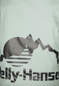 Tkanina mentolové barvy má velké černé logo s siluetami hor a horizontálními liniemi, což vytváří kontrastní designový prvek.