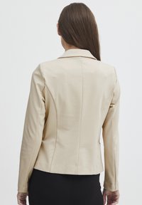 Beige strukturovaný blejzr s jednoduchým designem, s klopovým límcem a dlouhými rukávy. Hladký materiál, přiléhavý střih a minimální švy.