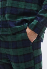 Zelena i mornarsko plava flanel košulja karo uzorka s opuštenim krojem, ima kopčanje na gumbe, duge rukave i vidljiv džep s glatkom teksturom.