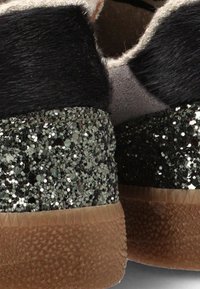 Pelo negro y tacones cubiertos de brillo sobre suelas de goma texturizadas. Presenta un upper suave, con un forro neutro y suave.