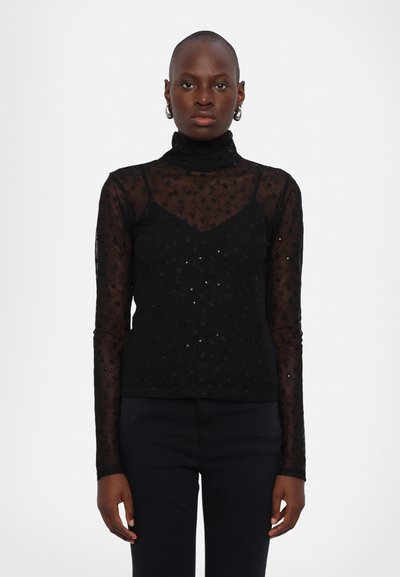 Top noir à manches longues avec un design transparent et texturé, orné de motifs floraux et de subtils sequins. Encolure montant, superposé sur un débardeur.