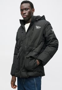 Mustapuffatakki, jossa on huppu, vetoketju, sivutaskut ja Reebok-logo. Sileä pinta ja tikattu muotoilu.