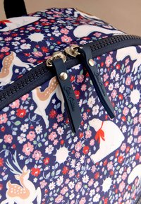 Mochila de tela azul marino con vibrantes patrones florales y de animales. Cuenta con cremalleras dobles plateadas con tiradores de tela azul y un asa resistente.