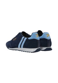 Un par de zapatillas azul marino con rayas y acentos en azul claro, con un logotipo dorado en el lateral y suelas blancas, vistas desde la parte trasera y lateral.