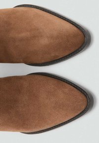 Botas de tobillo de ante marrón con punta afilada y suelas de goma negras, que presentan un sutil cosido a lo largo de los bordes para un detalle adicional.