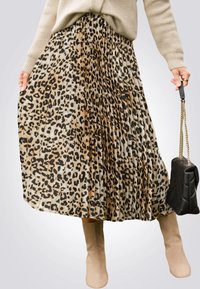Jupe plissée en imprimé léopard avec des motifs beige et noir. Le matériau semble doux ; associée à des bottes beiges longues jusqu'aux genoux et un sac à main noir.
