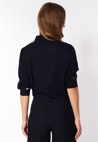 Czarna bluzka z podwiniętymi rękawami, kołnierzykiem i detalami guzików. Miękka tkanina i dopasowany krój, zestawiona z czarnymi spodniami z wysokim stanem.