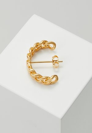 Złote, skręcone kolczyki koła z łańcucha, z prostym sztyftem i zapięciem w kształcie motylka, spoczywające na białej, ukośnej powierzchni.