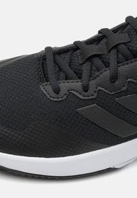 Chaussure de sport noire avec tige en maille texturée, bout arrondi et semelle blanche contrastante. Présente des lacets noirs et des accents de marque subtils.