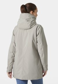 Chaqueta impermeable de color gris claro con capucha, que presenta una textura suave, mangas largas y puños ajustables.