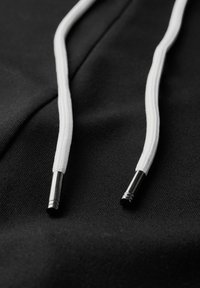Schwarzer Stoff mit weißen Kordeln. Strukturierte Oberfläche mit zwei Kordeln, die an den Enden glänzende metallische Enden haben.