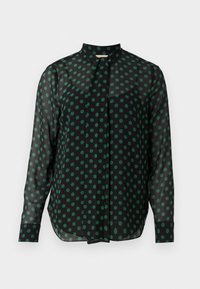 Blouse noire transparente à manches longues avec des pois verts, un col montant et une patte de boutonnage cachée à l'avant.
