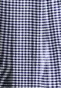 Μικρό καρό μοτίβο σε μπλε και λευκό ύφασμα με ελαφριές πτυχώσεις που δημιουργούν διακριτικές σκιές στην επιφάνεια του υφάσματος.