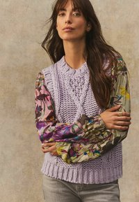 Pull en tricot lavande avec un corp texturé et des manches à motif floral multicolore. Il possède un col rond et un ourlet côtelé.