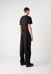 Svart t-skjorte med korte ermer kombinert med løse svarte bukser. Buksene har en baklomme med knapp. Teksturert stoff, minimalistisk design.
