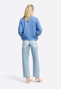 Maglione a maglia testurizzato di un azzurro chiaro con maniche ampie, abbinato a jeans a gamba dritta di un blu pallido con un motivo sottile. Scarpe beige con tacco basso.
