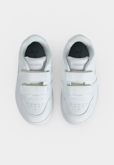 Двойка бели маратонки Lacoste с двойни велкро ленти, гледани отгоре на едноцветен фон.