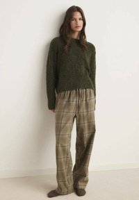 Pulover fuzzy verde măsliniu cu guler rotund, asortat cu pantaloni largi din tartan în nuanțe de bej, brun și albastru, completat de șosete închise la culoare.