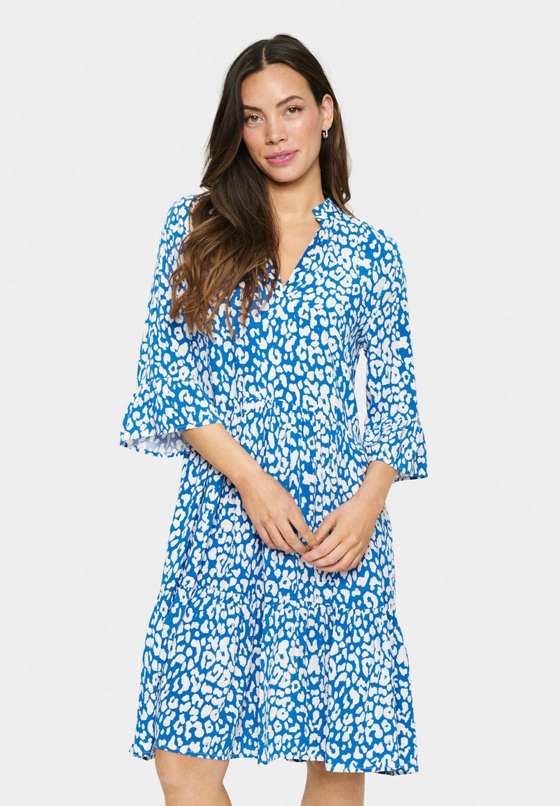 Vestido azul con estampado de leopardo blanco, escote en forma de V, mangas de campana de tres cuartos y dobladillo con volantes en varias capas. Confeccionado en una tela ligera.