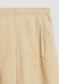 Pantalon décontracté beige clair avec une taille élastique et des poches latérales, présenté sur un fond uni gris clair.