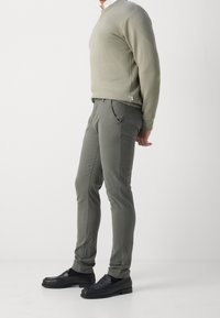 Felpa verde oliva con collo a giro, abbinata a pantaloni slim fit grigio chiaro e mocassini neri con texture intrecciata.