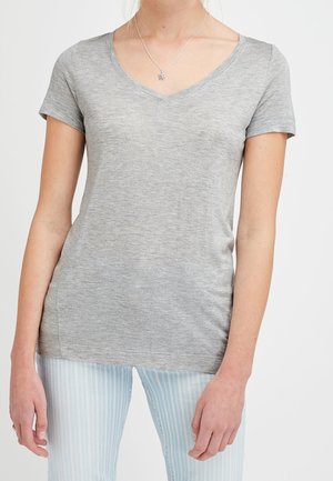 Person wearing a light grey short-sleeve V-neck shirt and light blue striped pants, showcasing casual clothing and a star necklace.