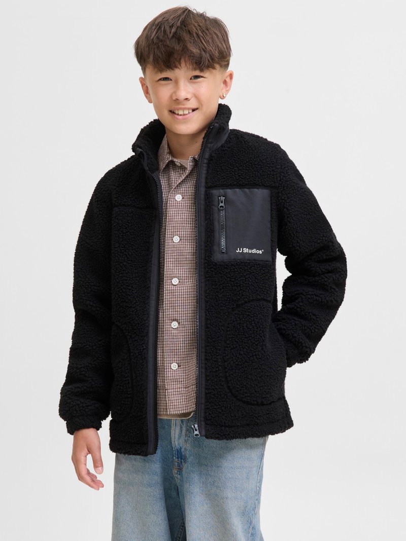 Black fleece jacket with a zippered chest pocket, featuring a contrasting smooth fabric accent. The design includes side pockets and a high collar.