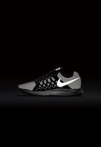 Zapatilla de running Nike en blanco y negro con el logo swoosh blanco, parte superior de malla texturizada y suela negra sobre un fondo oscuro.
