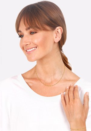 Gold chain necklace with a delicate twist design, resting on a bare collarbone. It complements a plain white shirt.