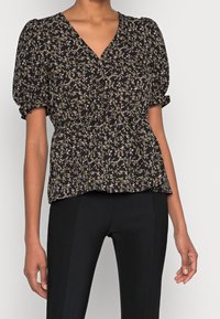 Blouse noire à motifs floraux avec un col en V, des manches bouffantes et une taille élastique. Présente de petites fleurs violettes et blanches sur un tissu doux.