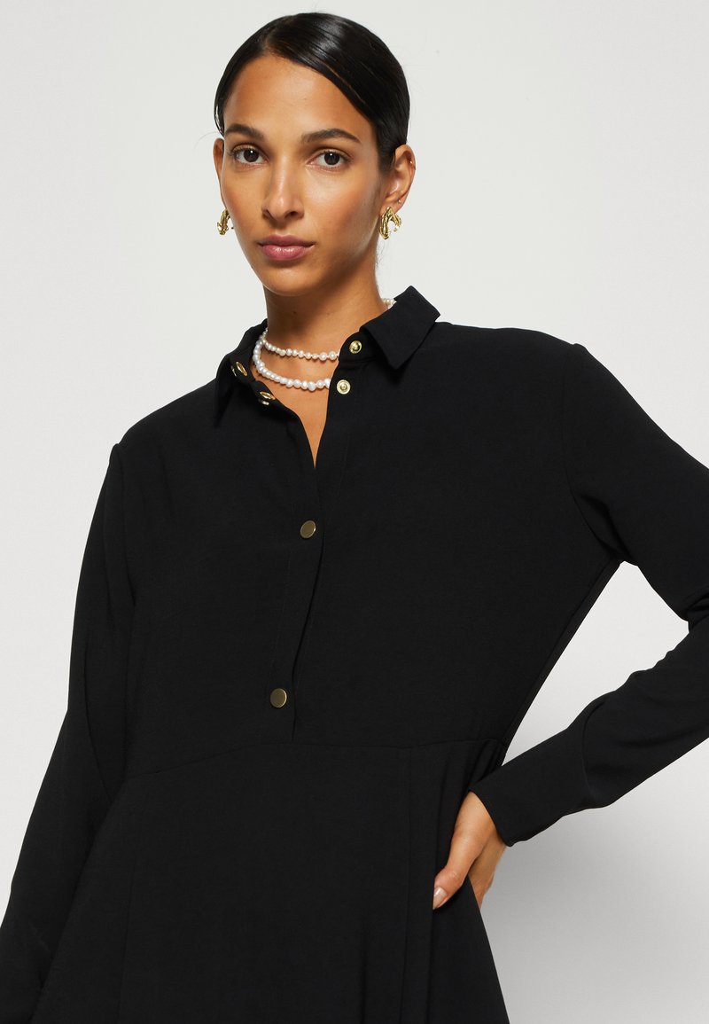 Schwarzes Langarmhemdkleid mit Kragen, ausgestattet mit goldenen Knöpfen und einem lockeren Schnitt. Glattes Gewebe mit A-Linien-Silhouette.