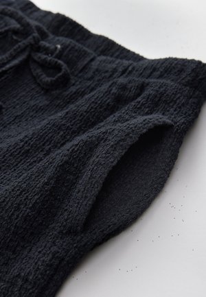 Czarne, teksturowane krótkie spodenki z prążkowanym wzorem, wyposażone w elastyczny pas ze sznurkiem oraz gładką podszewkę wewnętrzną.