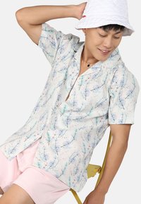 Chemise à manches courtes avec un motif floral aux couleurs claires ; fabriquée en tissu doux, elle présente un col à revers et une fermeture à boutons.