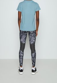 Person som står med ryggen mot kameran och bär svarta och gråmönstrade träningsleggings, ljusblå t-shirt, vita strumpor och svarta och vita sneakers.