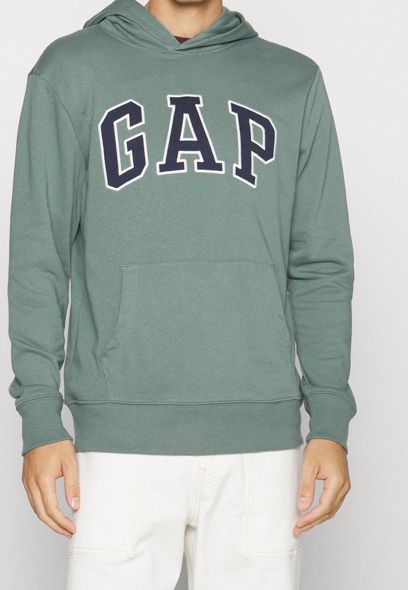Felpa verde con cappuccio, grande logo "GAP" blu navy, coulisse sul cappuccio, tasca frontale e polsini e orlo a costine, realizzata in morbido tessuto misto cotone.