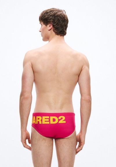 Rožinės maudymosi glaudės su geltonu užrašu "DARED2", pagamintos iš elastingos medžiagos ir formuojančios kūną.