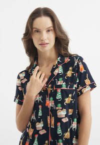 Granatowe piżamy z krótkimi rękawami, z zabawnym wzorem kotów w różnych kolorach, z różowym wykończeniem i kieszonką z przodu.