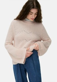Helles rosa gestricktes Sweatshirt mit strukturiertem Muster, hohem Kragen und ausladenden Ärmeln, kombiniert mit blauen High-Waist-Jeans.