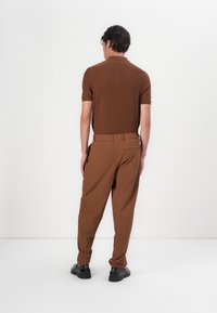 Brown knitted polo shirt paired with brown tapered trousers. The outfit features a relaxed fit and solid color with a subtle texture.