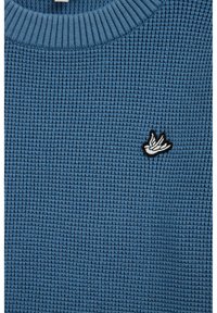 Pull bleu en maille gaufrée avec encolure côtelée et petit logo brodé blanc et noir sur le côté gauche. Texture douce, épaisseur moyenne.