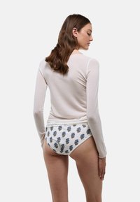 Haut crème à manches longues associé à un slip blanc orné de broderies florales bleues. Les tissus semblent doux et légers.