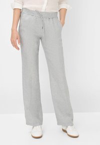 Pantalon en lin gris clair avec une coupe décontractée, taille élastique et fermeture à cordon. Porté avec des baskets blanches, présente une surface texturée.