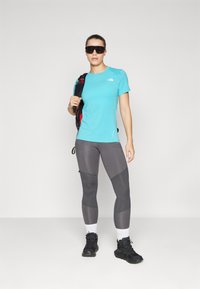 T-shirt de sport bleu clair, leggings gris avec des détails en panneau, bottes de randonnée noires et un sac à dos noir avec des accents rouges.