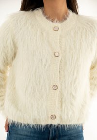 Cardigan di crema fluffy con cinque bottoni, dotato di hardware dorato e design a maglia testurizzata. Vestibilità rilassata e tessuto morbido e voluminoso.