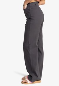 Black wide-leg pants with a high waist, made from durable cotton material, featuring side pockets and a straight cut. Paired with slide sandals.